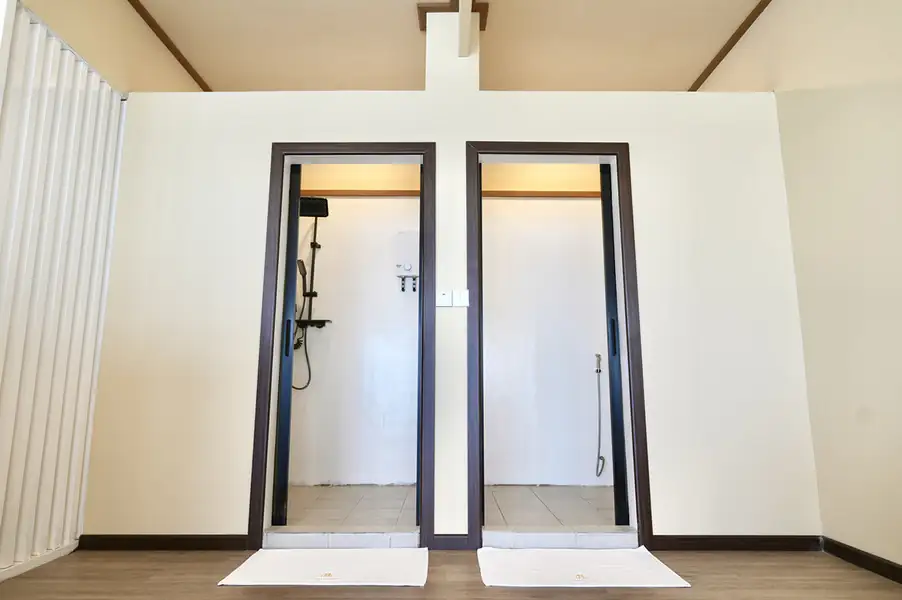 A bright bathroom at F Lina Water Villa Resort featuring a white vanity desk, round mirror, white toilet, patterned floor tiles, and a glass-enclosed electric shower.