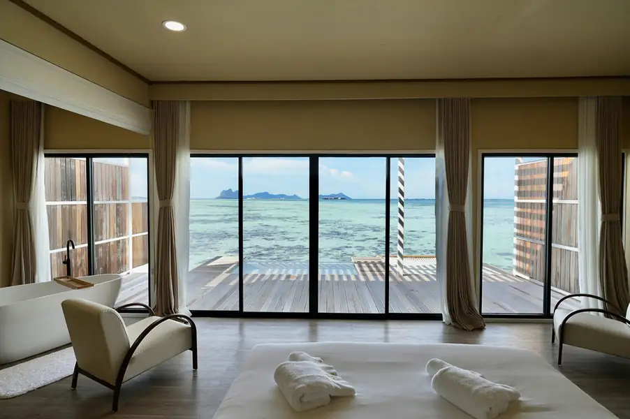 A spacious bedroom offering a comfortable bed, an in-room bathtub, and wide glass doors opening to a balcony with a panoramic seaview over the Celebes Sea, reflecting elegant local architecture at F-Lina Water Villa Resort.